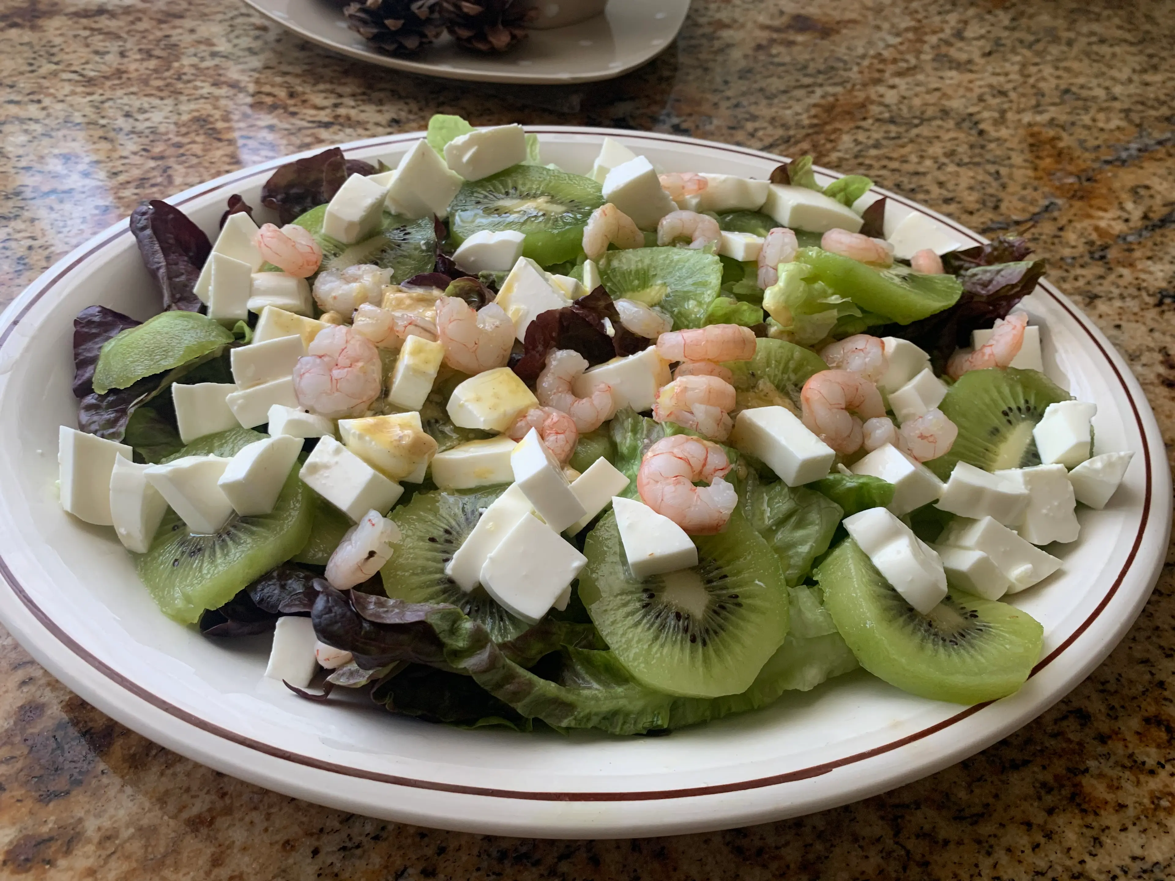 Step <p>Colocamos la lechuga en una fuente y distribuimos encima las rodajas de kiwi, el queso de Burgos y las gambas reservadas. Regamos con la vinagreta y servimos</p> illustration