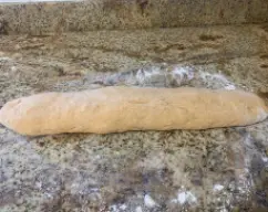 Step <p>Retire la masa sobre una superficie espolvoreada con harina. Forme un cilindro y, con la espátula o un cuchillo, corte 10 porciones de aprox. 70-75 g. Deles forma de bola procurando que la parte superior quede bien tensionada y lisa y colóquelas en la bandeja preparada. Pincele con el huevo batido y deje reposar en un lugar templado libre de corrientes de aire hasta que doblen su volumen (aprox. 30 minutos). </p> illustration